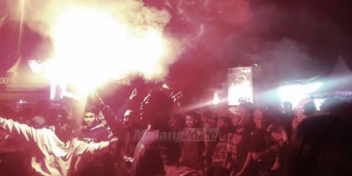 Aremania menyalakan flare saat nonton bareng di depan Stasiun Kota Baru, Malang.