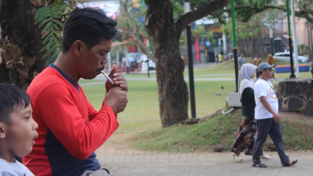 Seorang perokok sedang menyalakan sebatang rokok di tempat duduk yang berada di tengah Alun-alun Merdeka, Kota Malang. Alun-alun Merdeka masuk kawasan bebas rokok.(Miski)