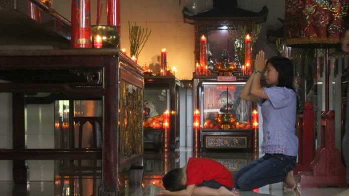 Umat konghucu khusyuk beribadah mengajak serta anaknya di Kelenteng Kwan Im Tong Kota Batu, Jumat (16/2). (Aziz / MVoice)