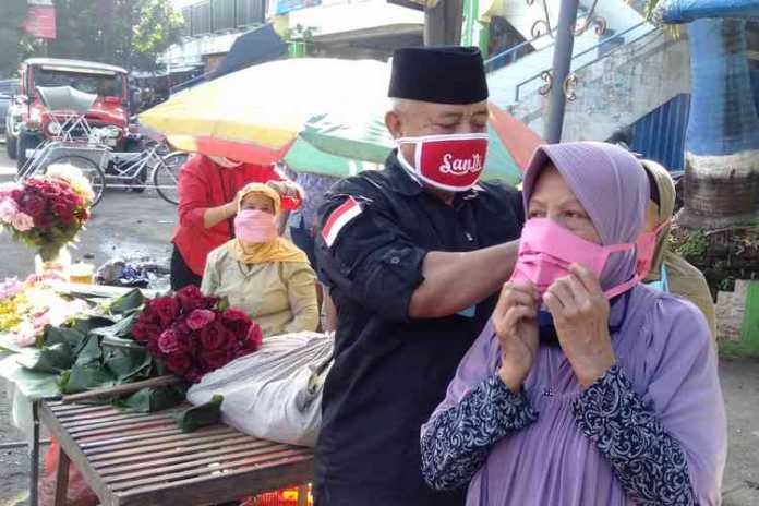 Bupati Malang HM Sanusi saat memberikan dan memakaikan masker ke warga di pasar Kepanjen. (Toski D)
